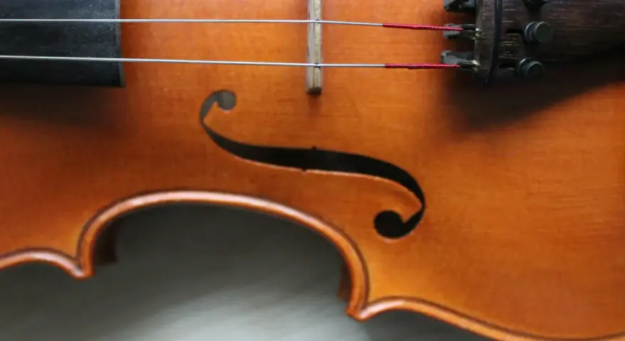 Drewniany korpus skrzypiec, z widocznymi strunami i mostkiem. Ten instrument, być może nawet stradiwarius, emanuje historią i pięknem.