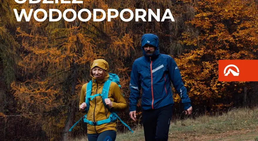 Para idzie przez jesienny las w odzieży wodoodpornej. To oferta firmy Northfinder, która specjalizuje się w odzieży outdoorowej.