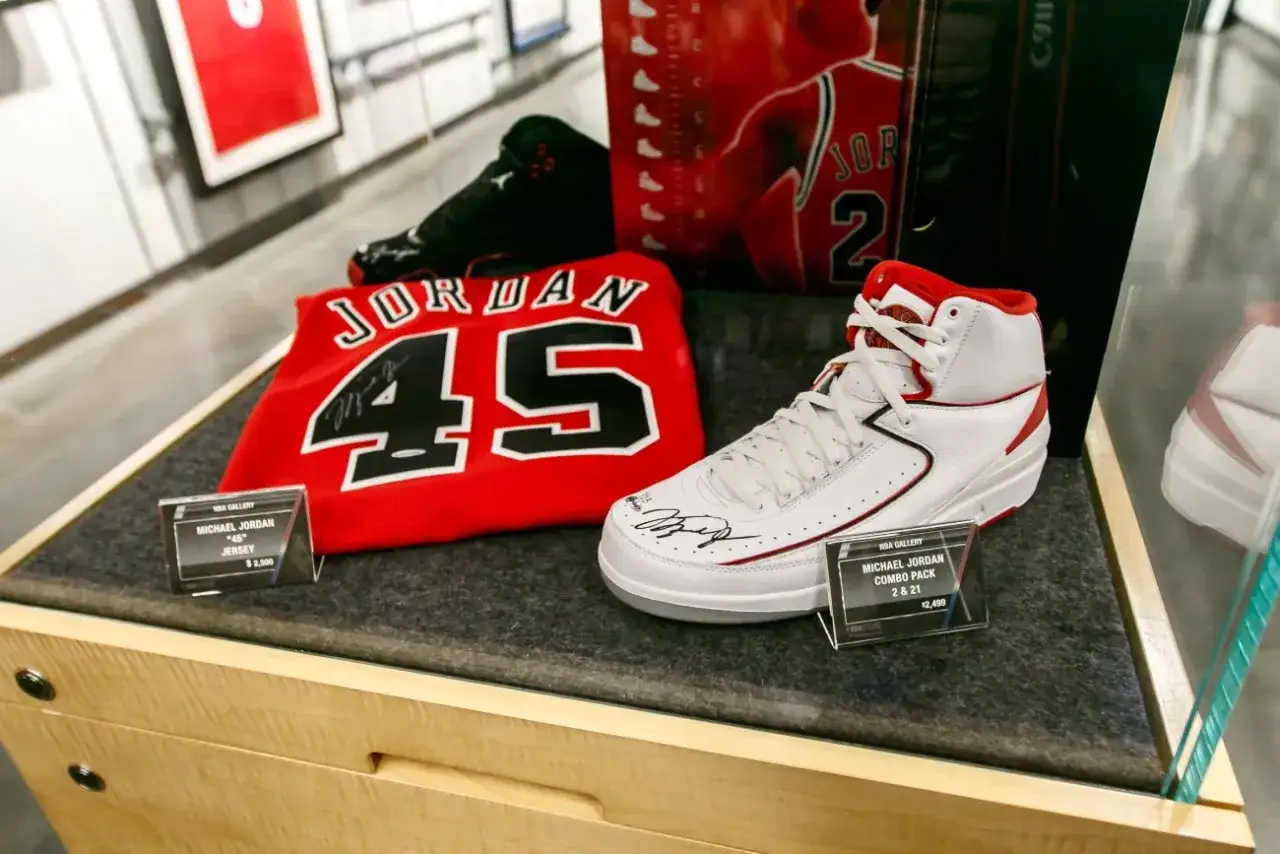 Białe buty sportowe z czerwonymi akcentami, podpisane przez Michaela Jordana, obok koszulki z numerem 45. Michael Jordan rozmiar buta to marzenie kolekcjonerów.