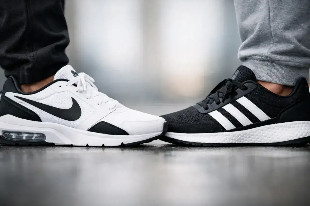Białe buty Nike i czarne buty Adidas stoją naprzeciw siebie, symbolizując rywalizację marek.