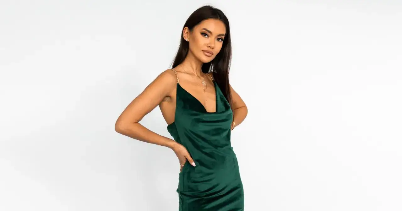 Modelka w szmaragdowej sukience z weluru, zmysłowo prezentuje jakie dodatki do zielonej sukienki pasują, podkreślając elegancję.