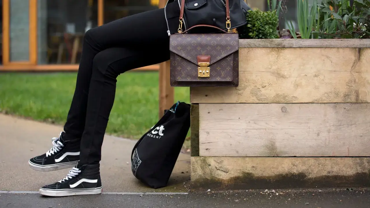 Osoba w czarnych rurkach i klasycznych Vansach, z torbą Louis Vuitton. Vans co to za firma? To marka znana z kultowych trampek.