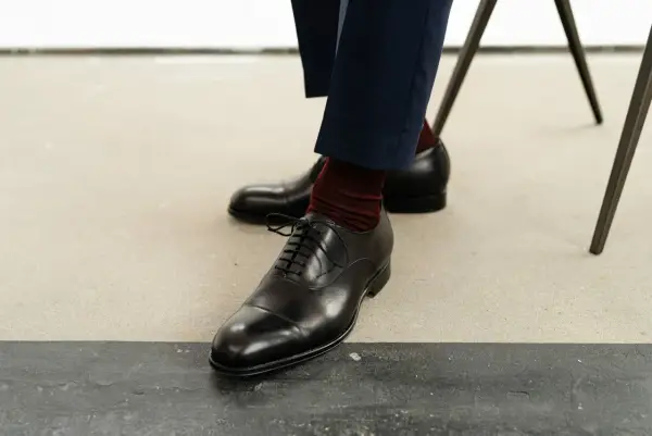 Eleganckie czarne buty męskie, rozmiar buta 50, z bordowymi skarpetkami i granatowymi spodniami.